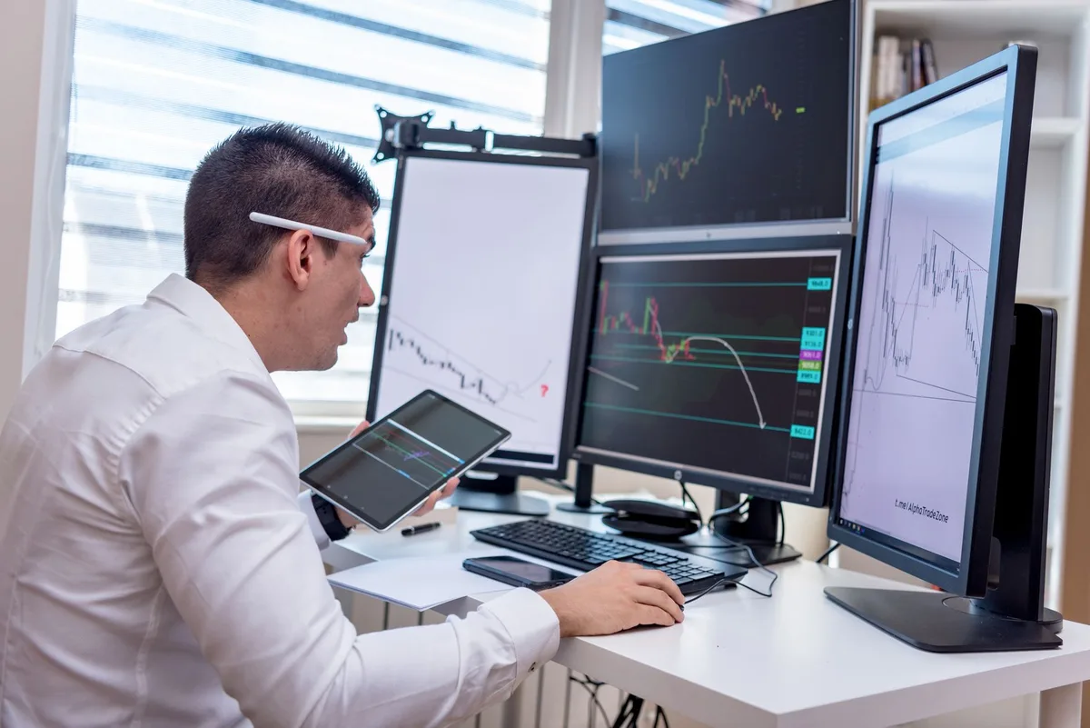 Multiple computer screens displaying stock market data and financial charts