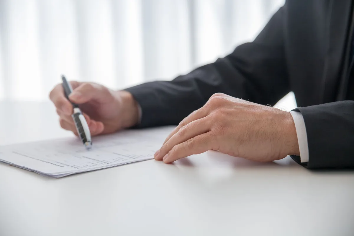 Person signing property purchase contract on desk