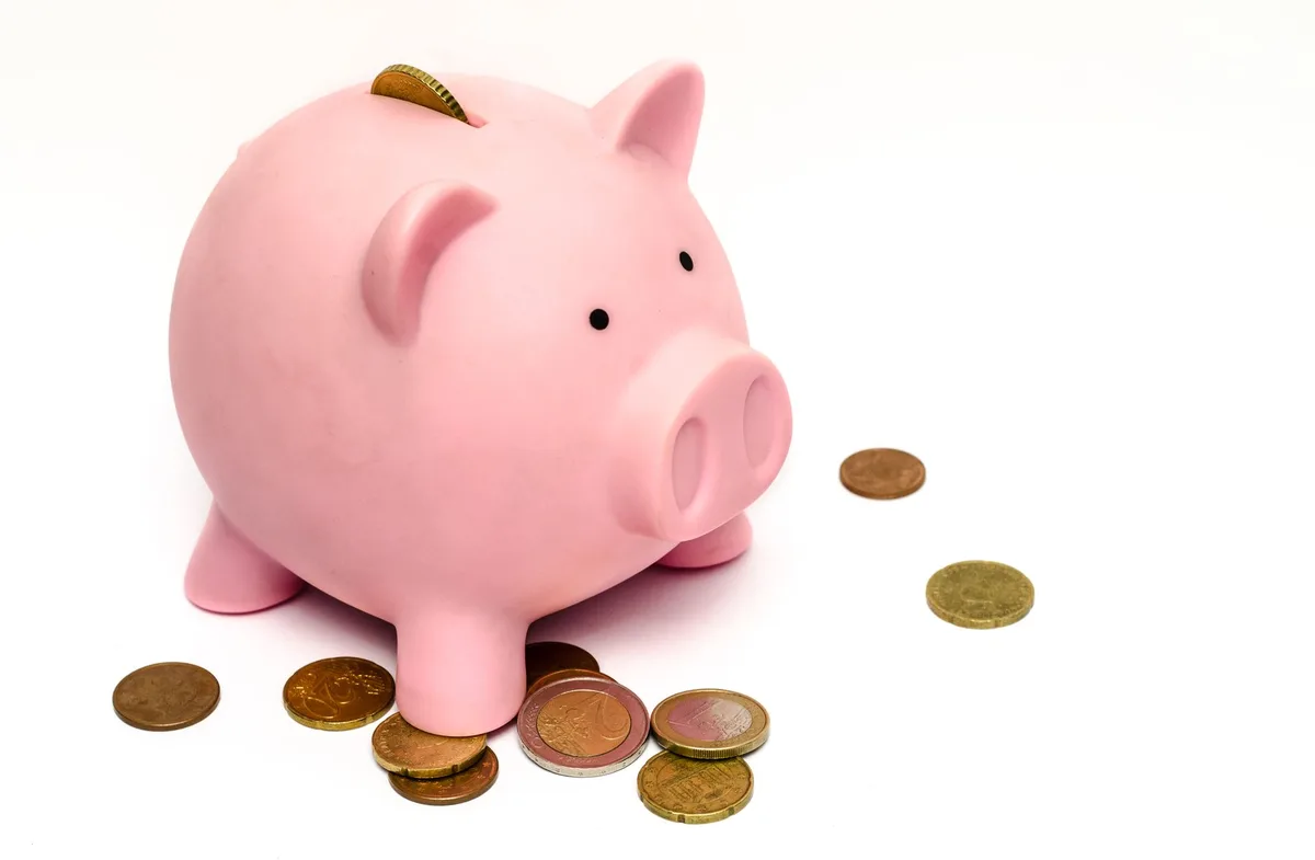 Pink piggy bank with stacked coins on a wooden surface, representing personal savings and budget planning