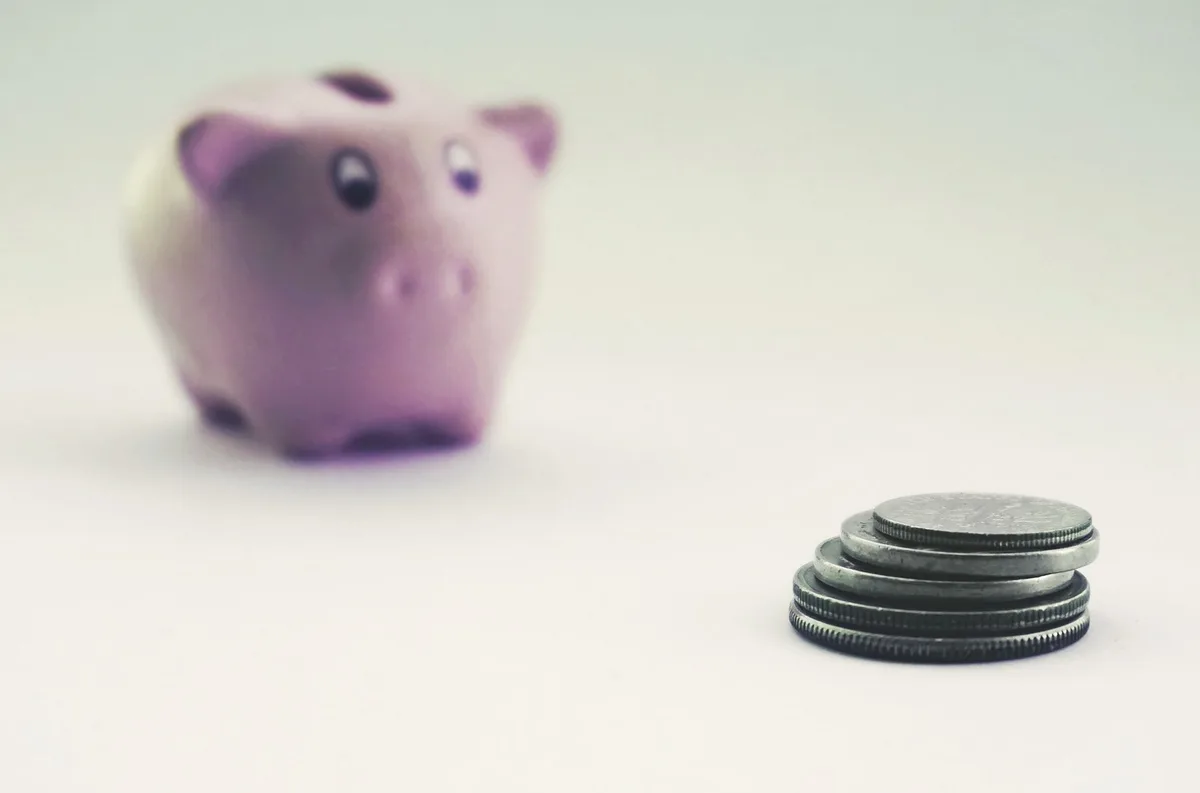 Pink ceramic piggy bank beside stacked coins representing emergency fund savings